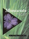 The cover image of Monocots: Systematics and Evolution, featuring a purple flower against a plain black background, set into a cover of tall green gra The cover image of Monocots: Systematics and Evolution, featuring a purple flower against a plain black background, set into a cover of tall green gra