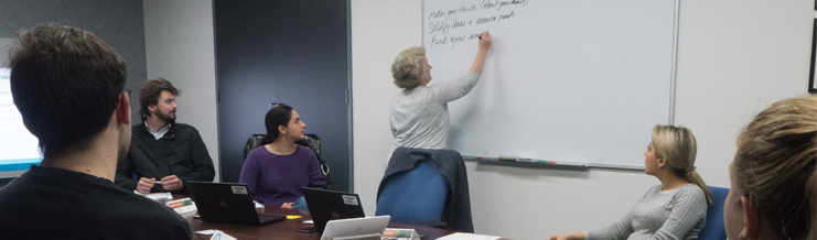 A group of people sitting looking towards a teacher writing on the wall